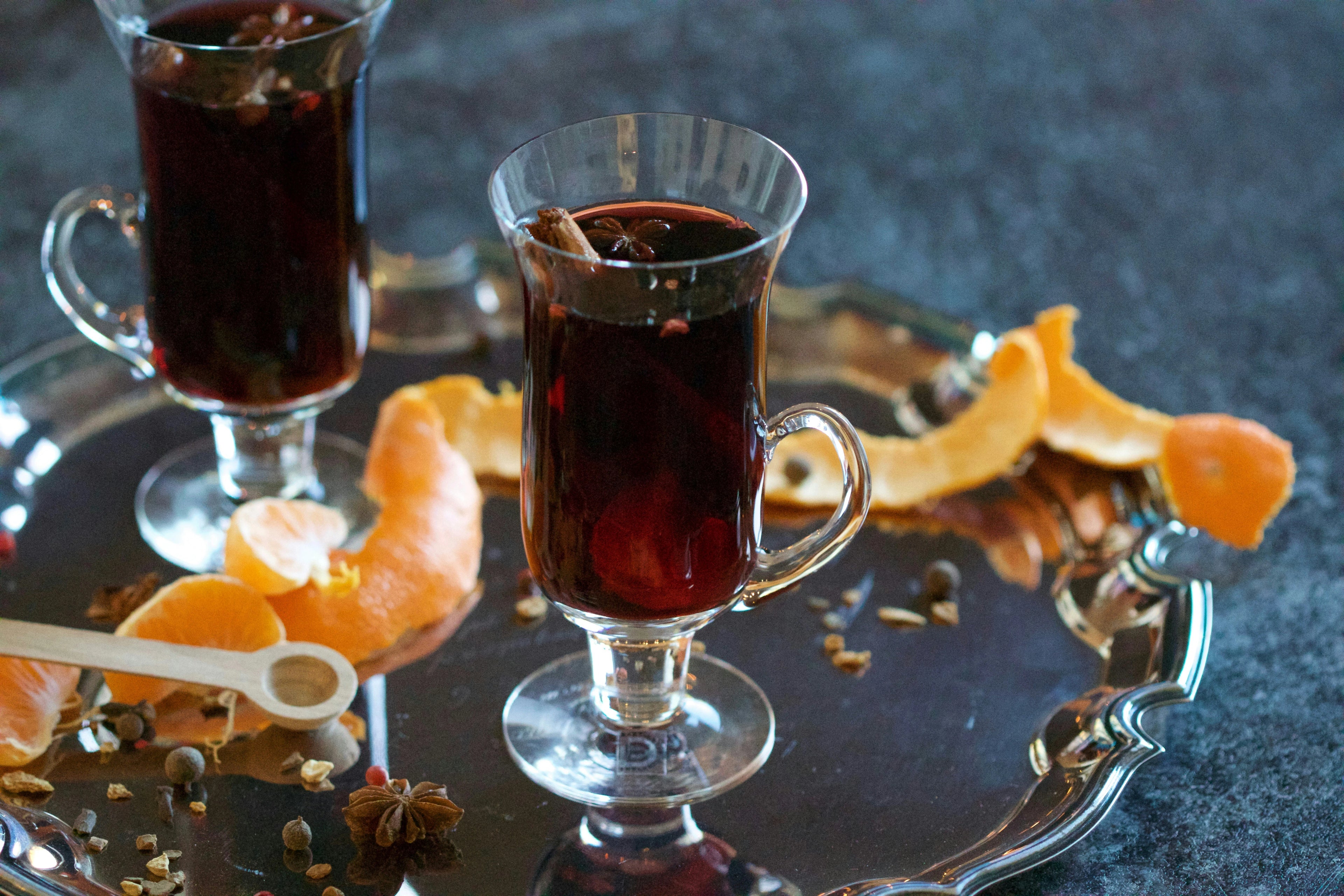 Two glasses of mulled wine on a silver tray with orange peels and spices.
